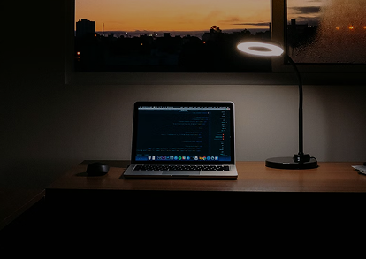 There is a laptop on a desk and it is dark outside.